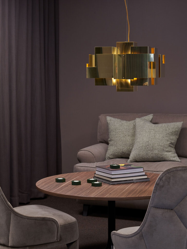 Elegant hörna i Klaraviks lokaler med modern guldlampa, grå sammetsstolar och matchande mörklila väggar.